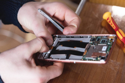 一个家庭工匠修理拆散的智能手机的手的特写镜头。家庭自修电子产品的概念
